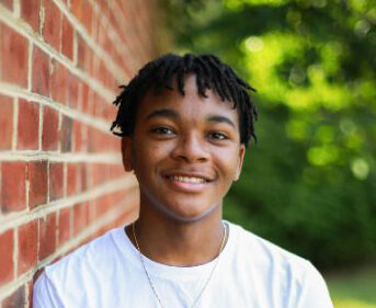 Smiling teen with braces leaning against a brick wall